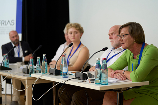 Fünf Personen sitzen auf der Bühne. Vor ihnen sind auf einem Tisch Mikrofone aufgestellt. 